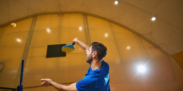 Focused tennis player firmly gripping the racket with his hand while jumping high to hit the ball